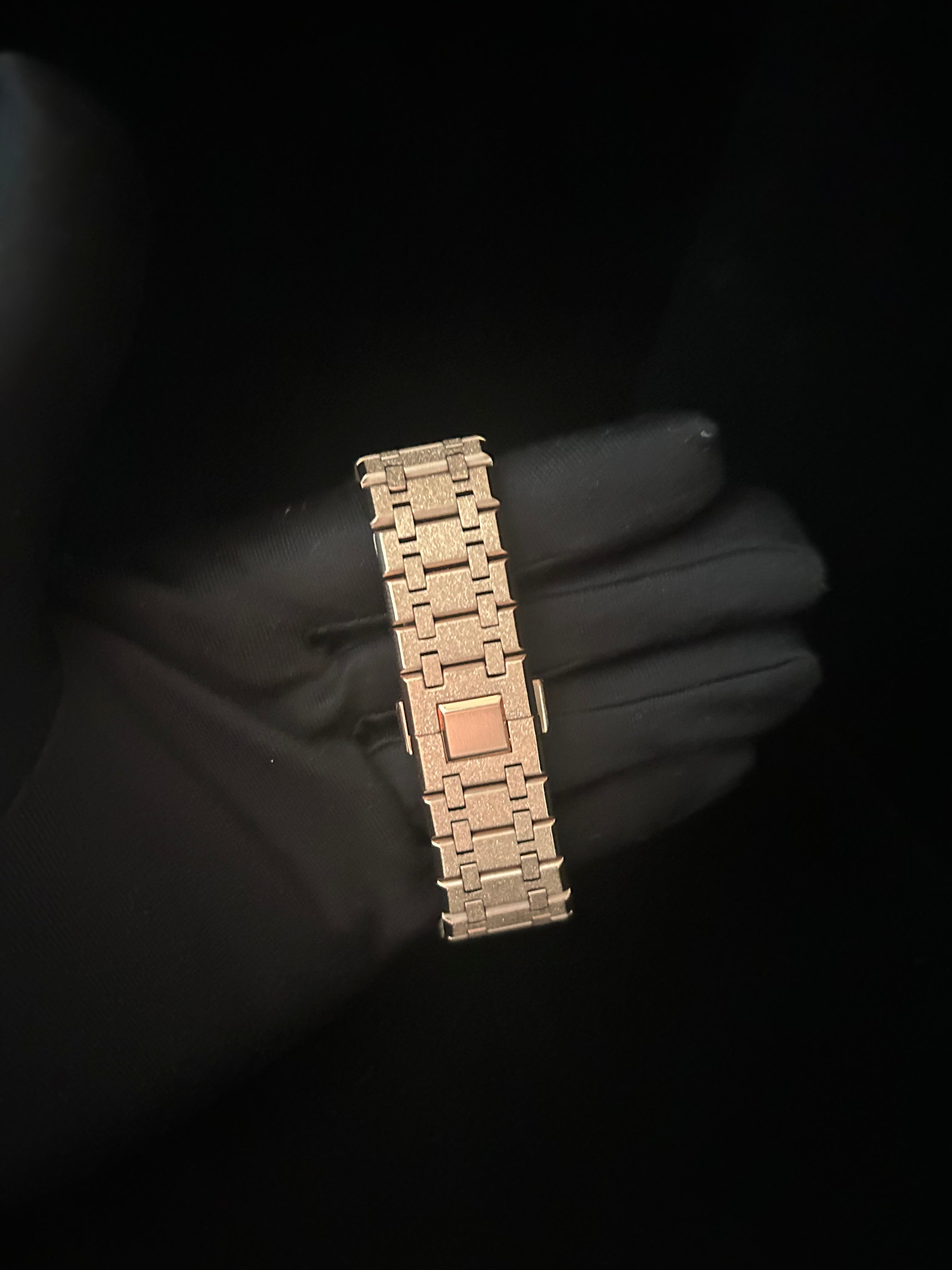 Gold bracelet held by a gloved hand against a black background