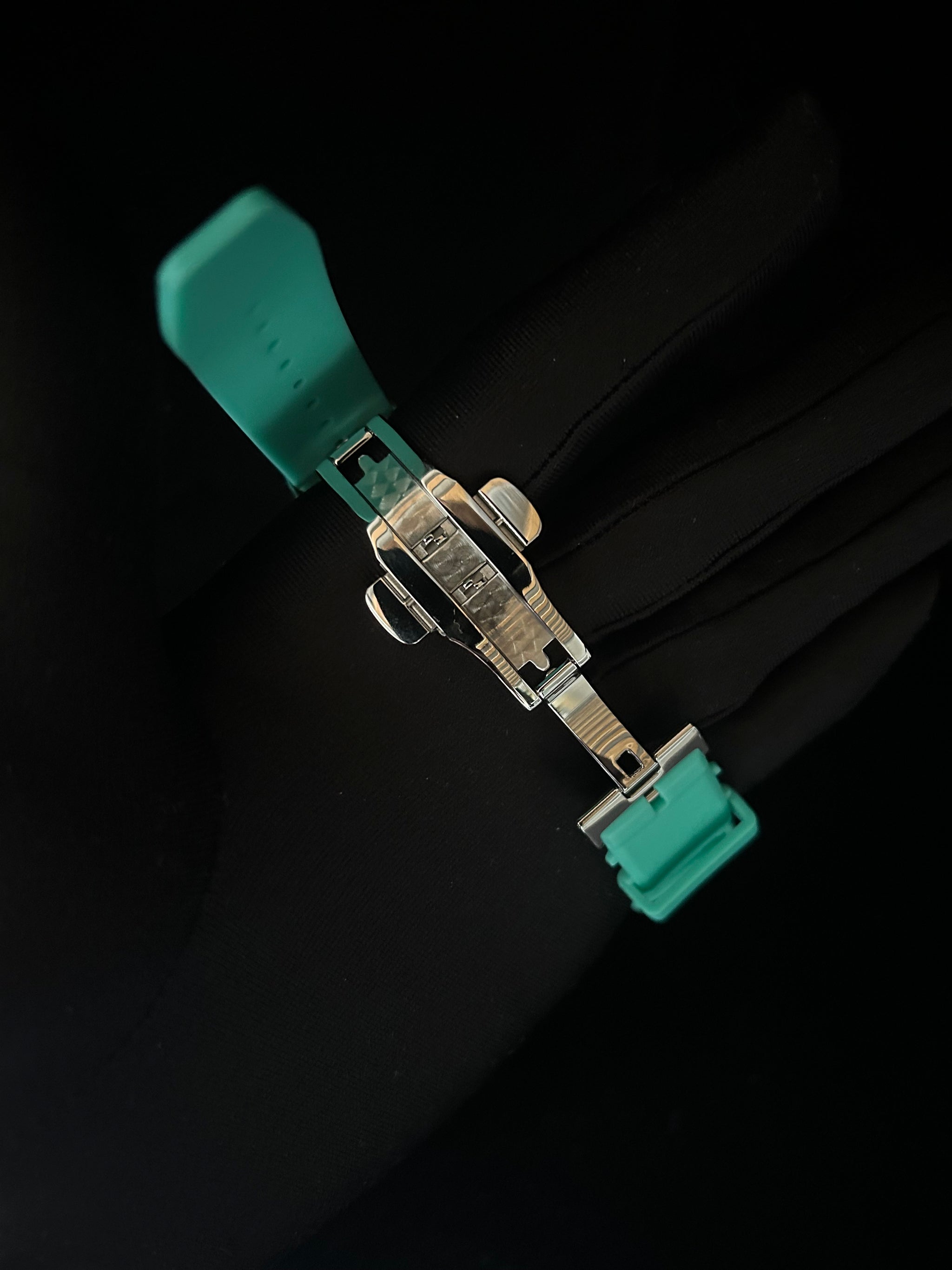 Teal watch strap with metal clasp on a black background