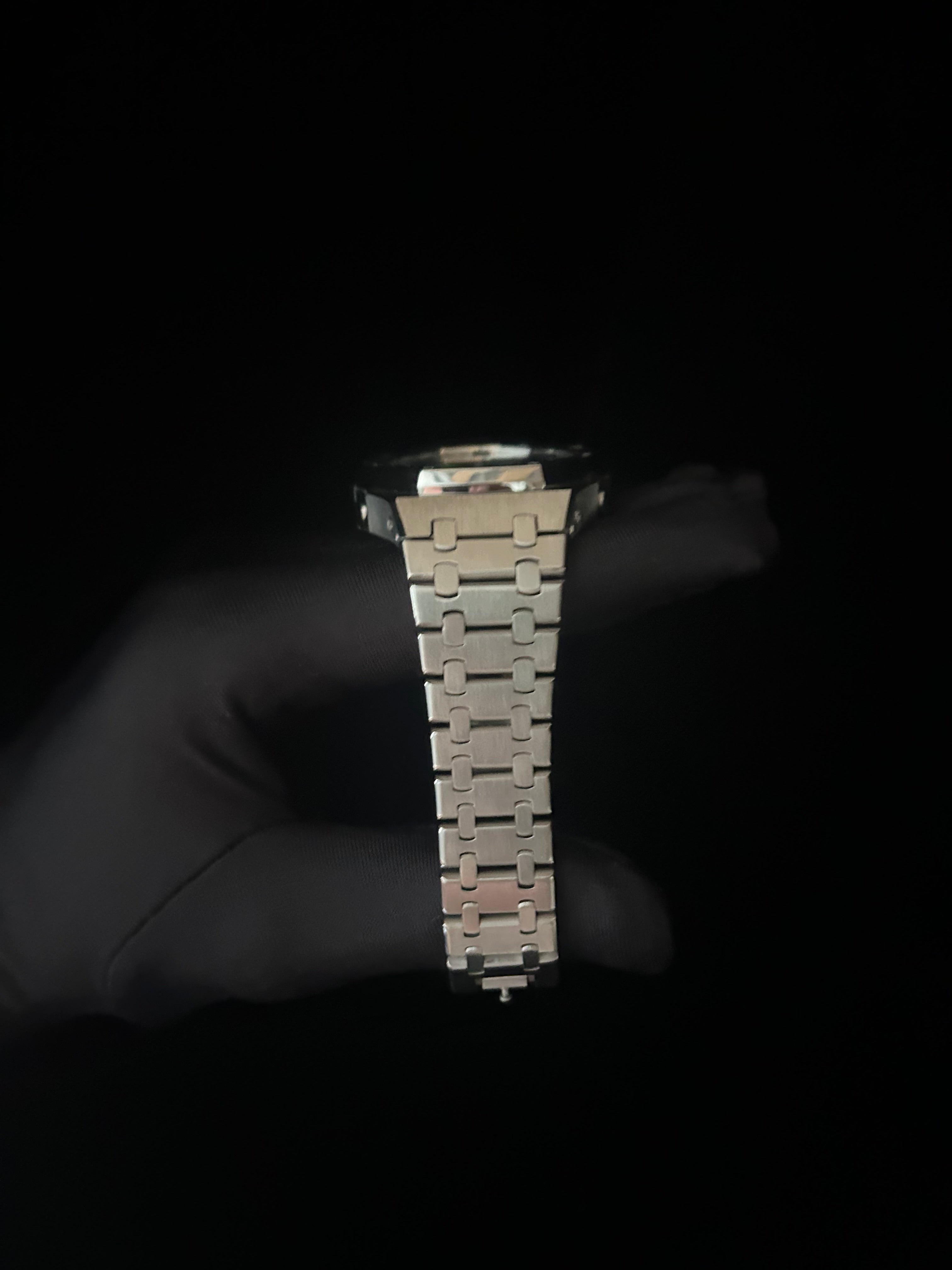 Metallic watch strap held by a gloved hand against a black background