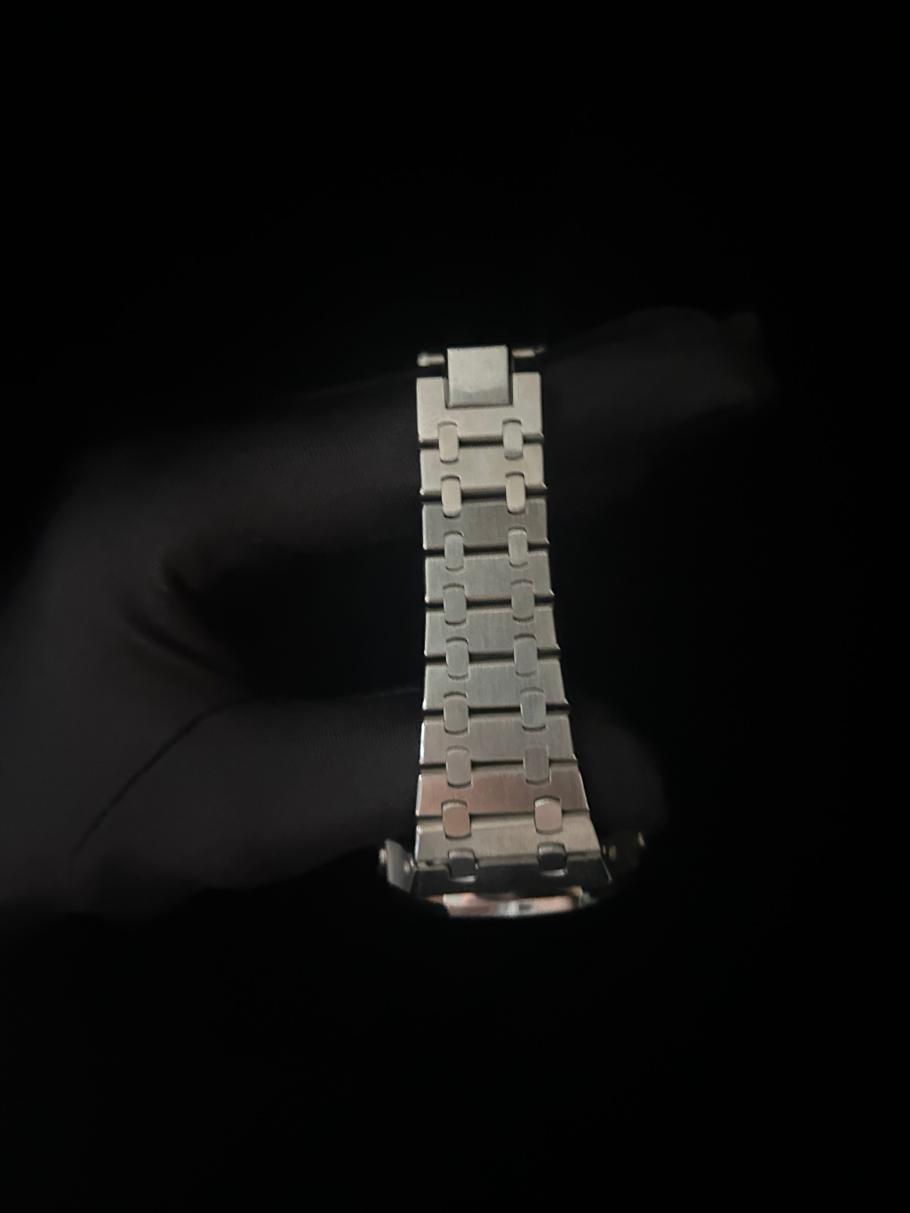 Metallic watch band held by a gloved hand against a black background