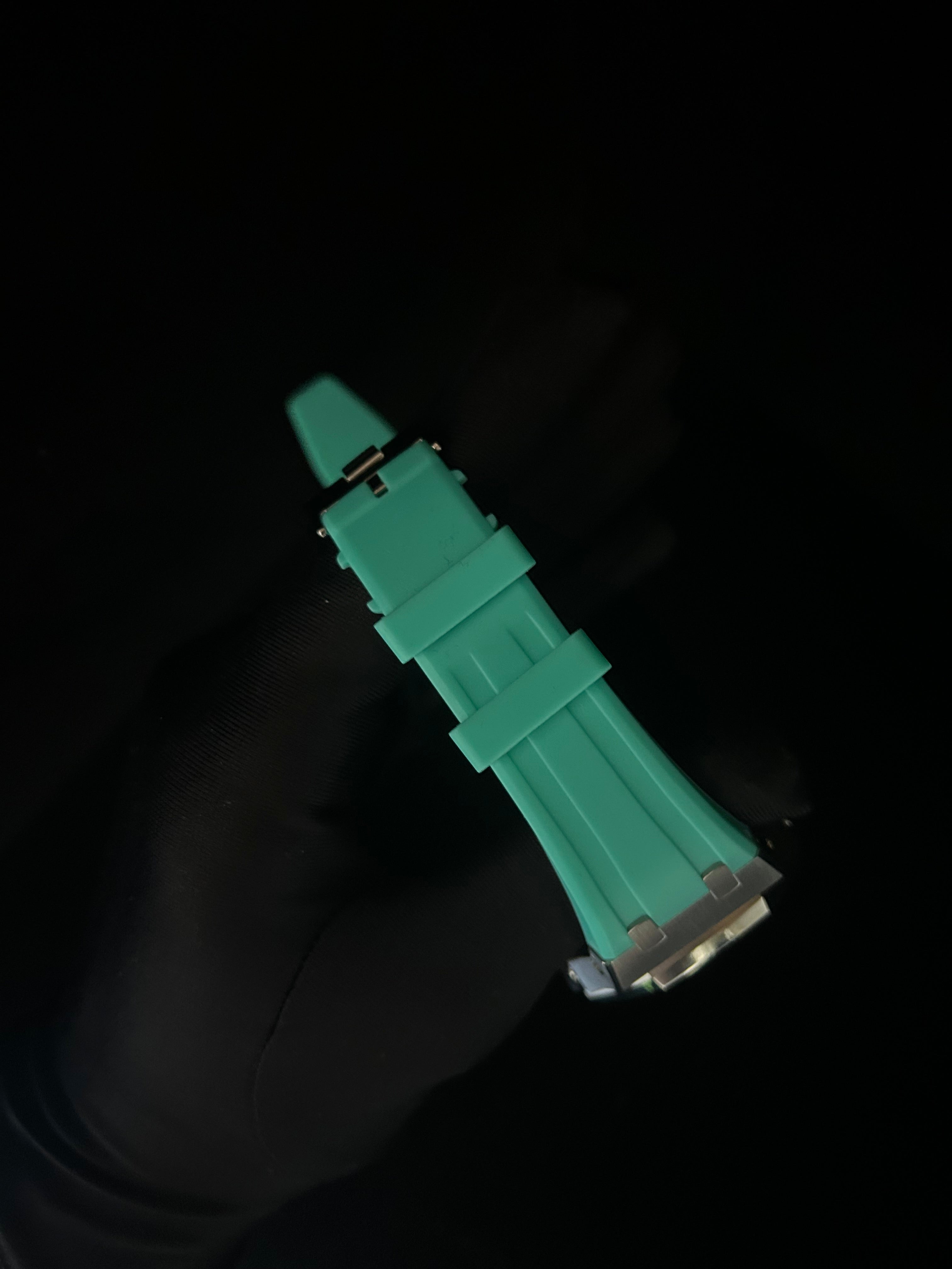 Green watch strap held by a gloved hand against a black background