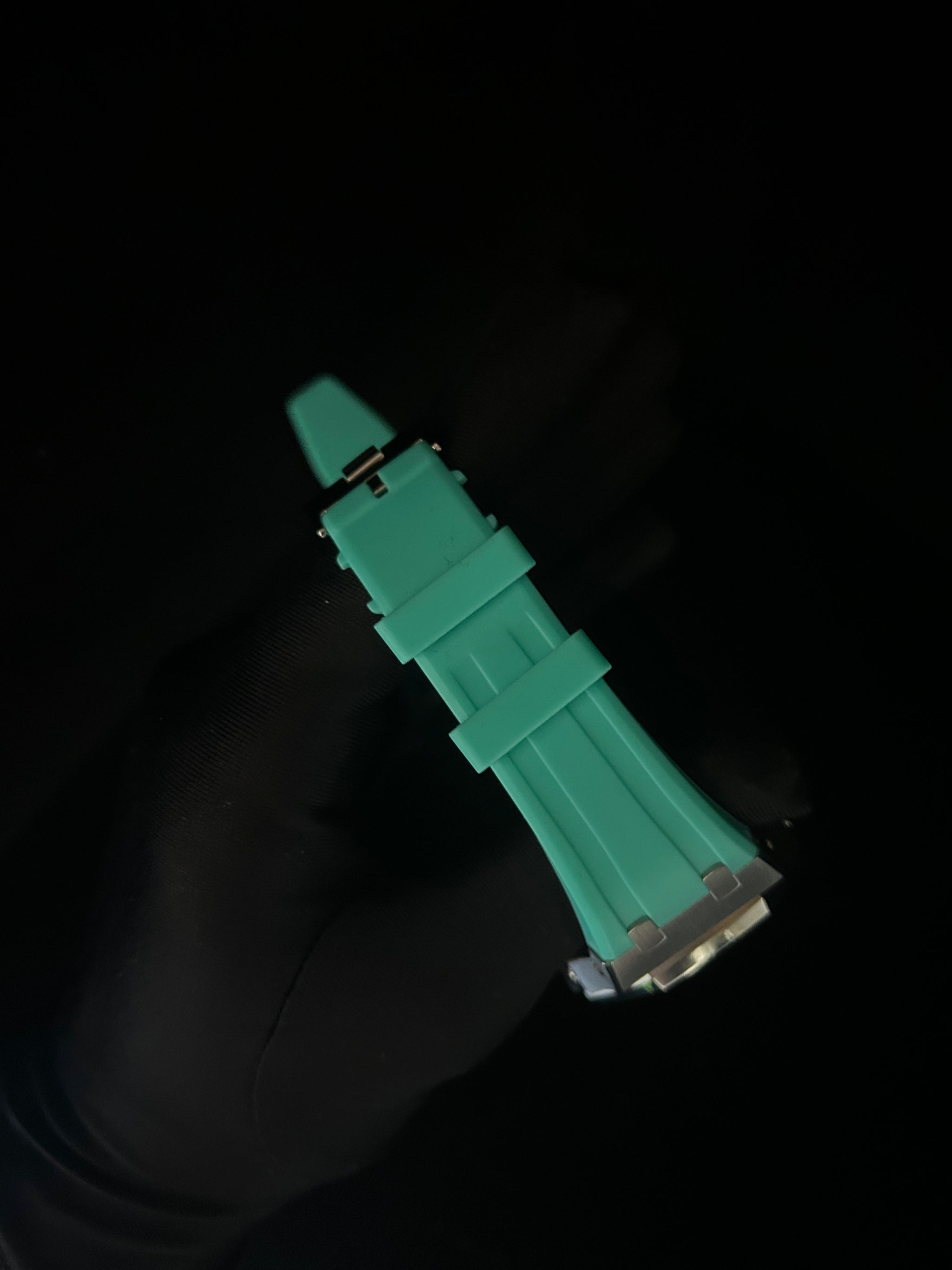 Green watch strap held by a gloved hand against a black background