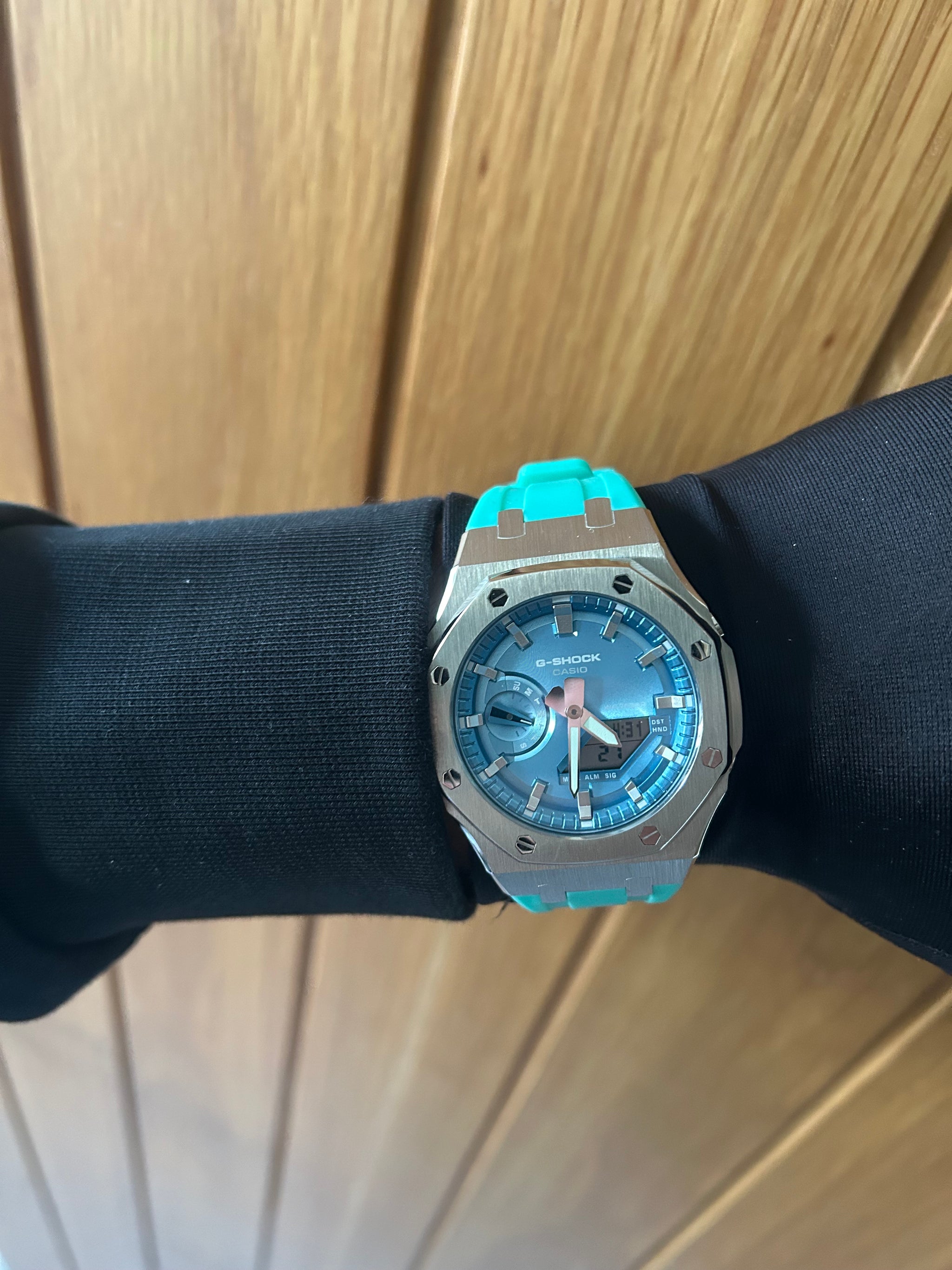 Luxury watch with a blue face and silver case on a black stand against a wooden background