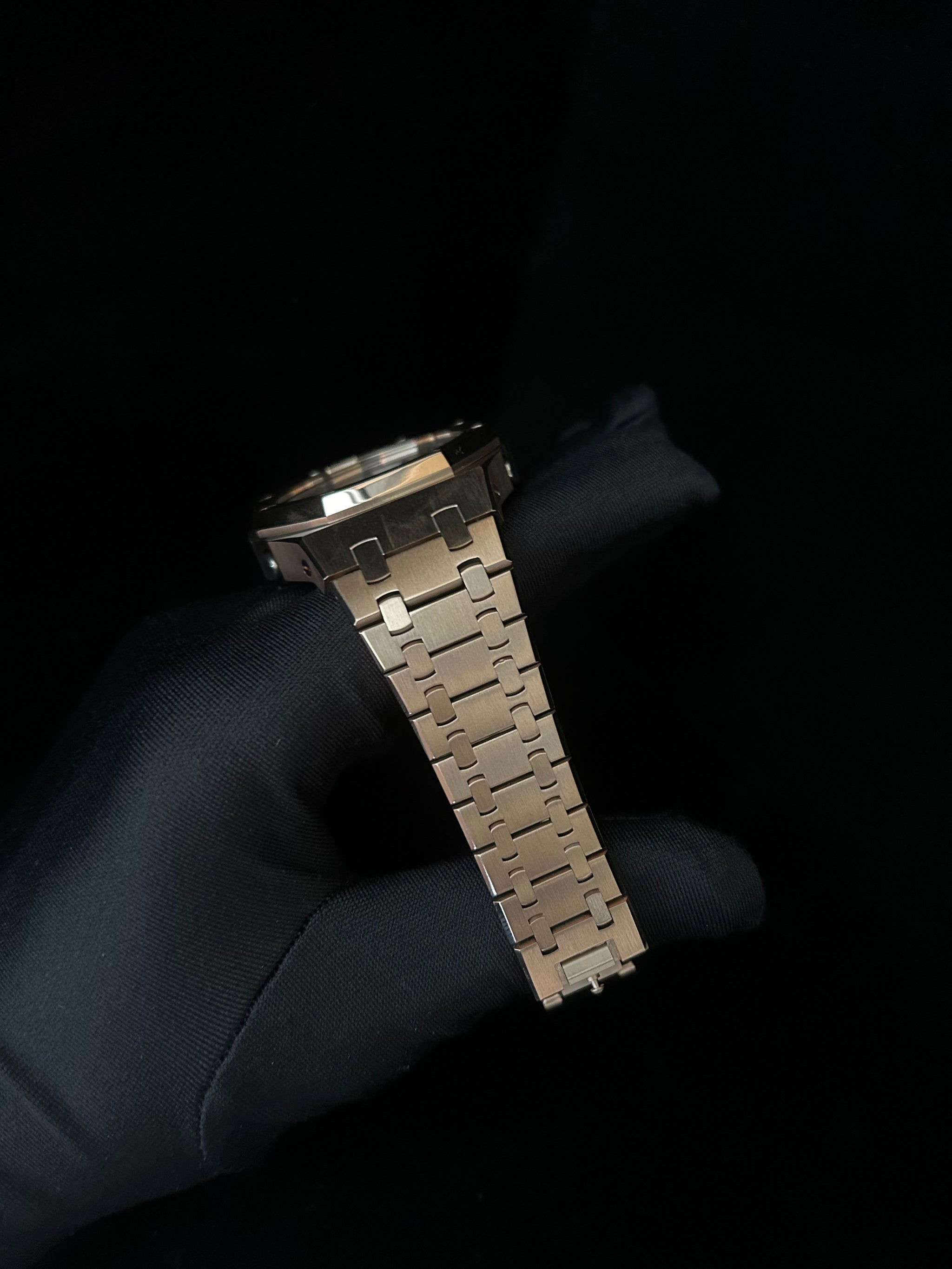 Metallic watch strap held by a gloved hand against a black background