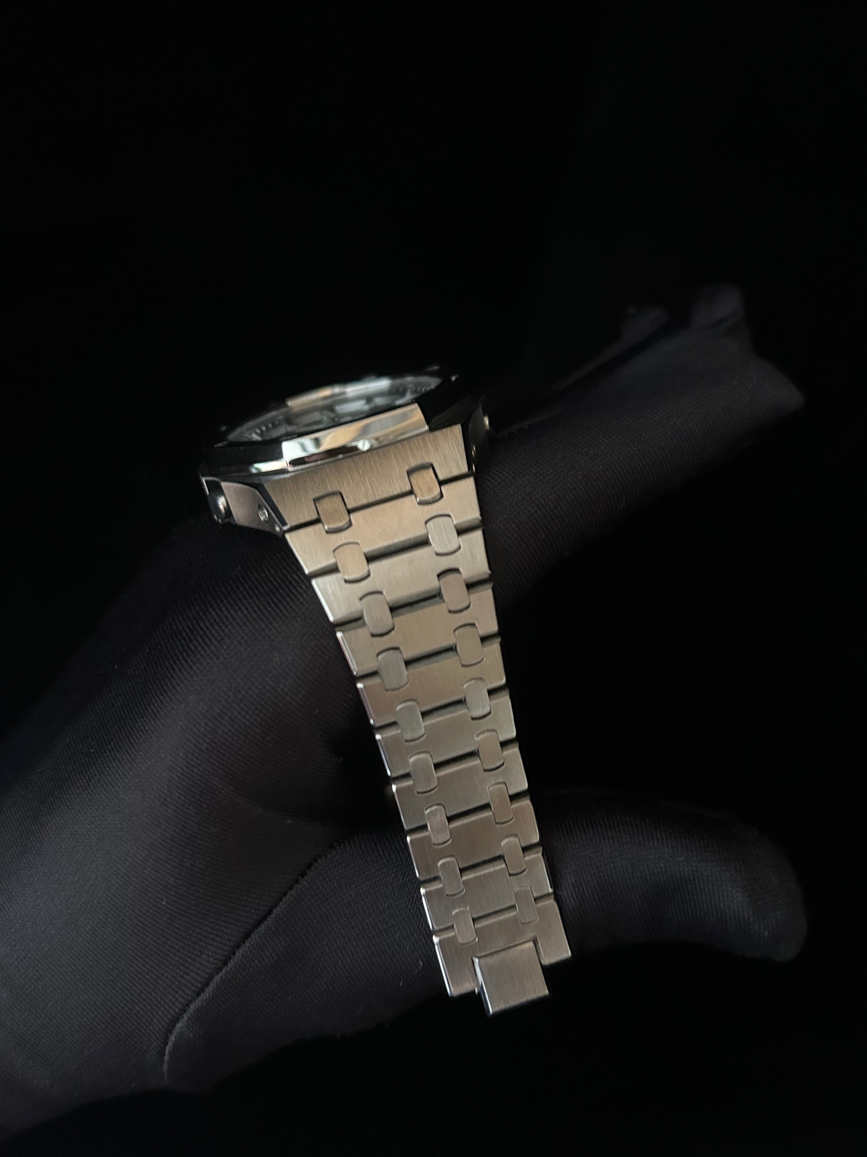 Metallic watch strap held by a gloved hand against a black background