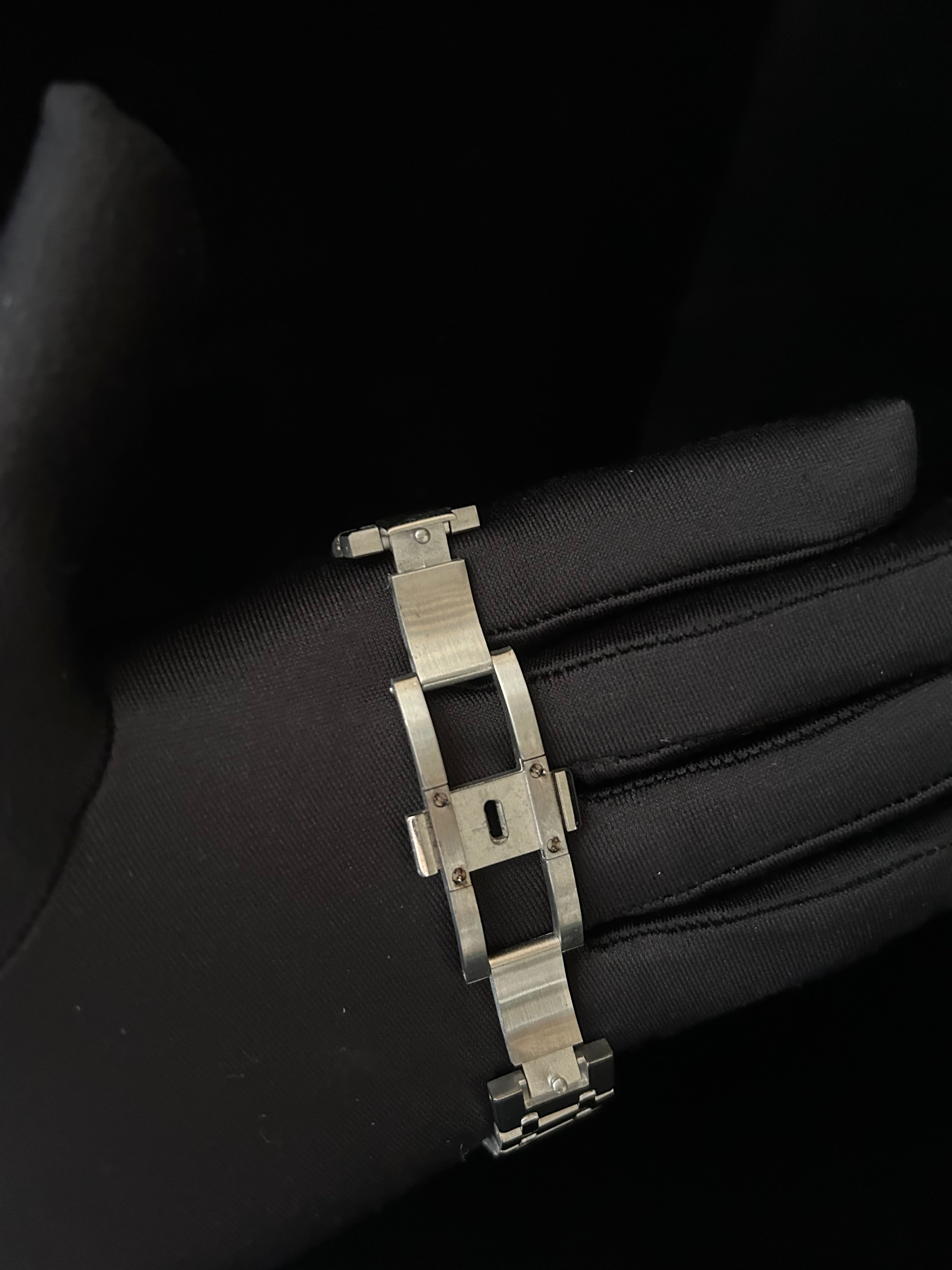 Metallic bracelet on a black glove against a dark background