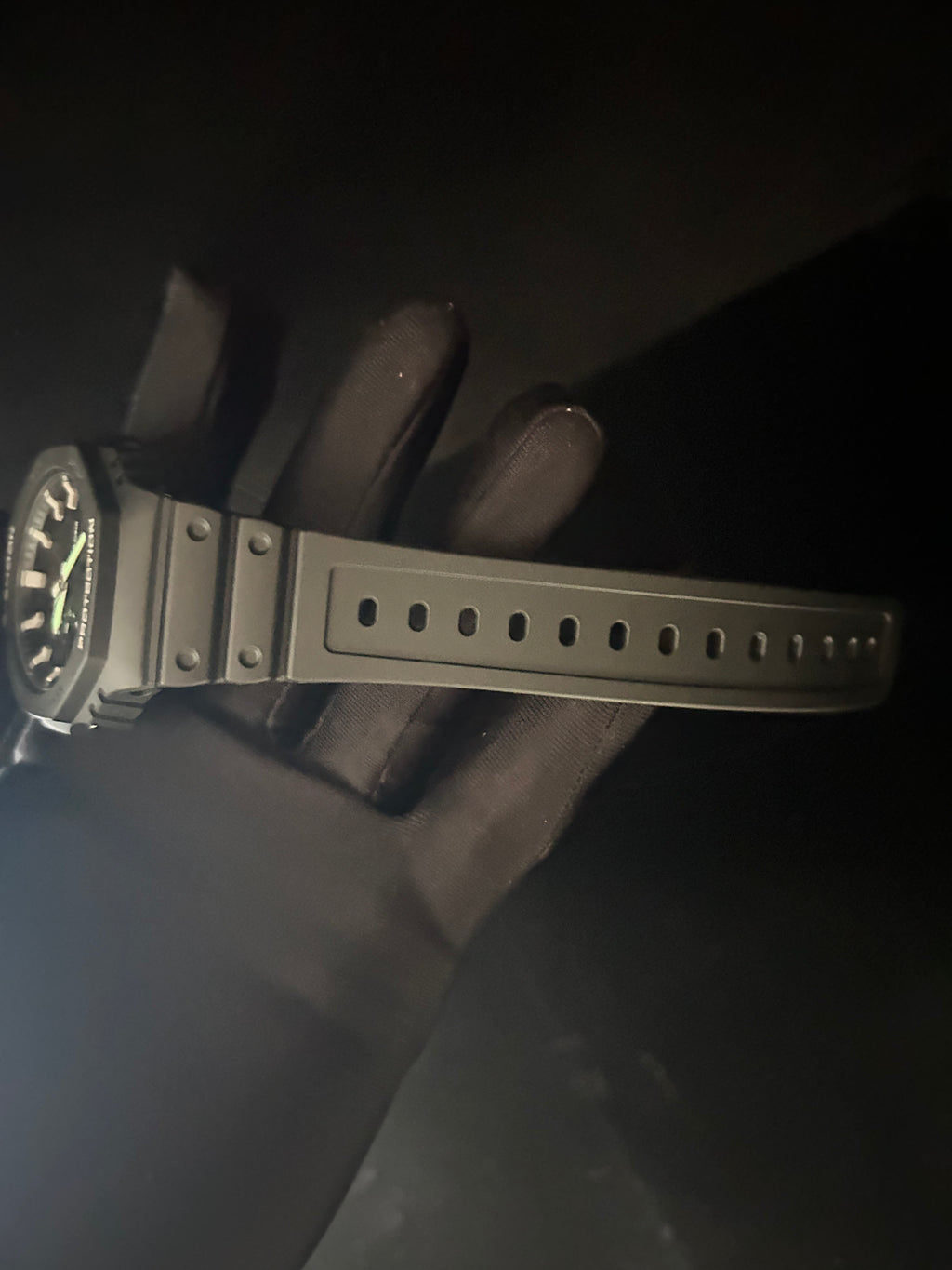 Black wristwatch with a textured strap held by a gloved hand against a dark background