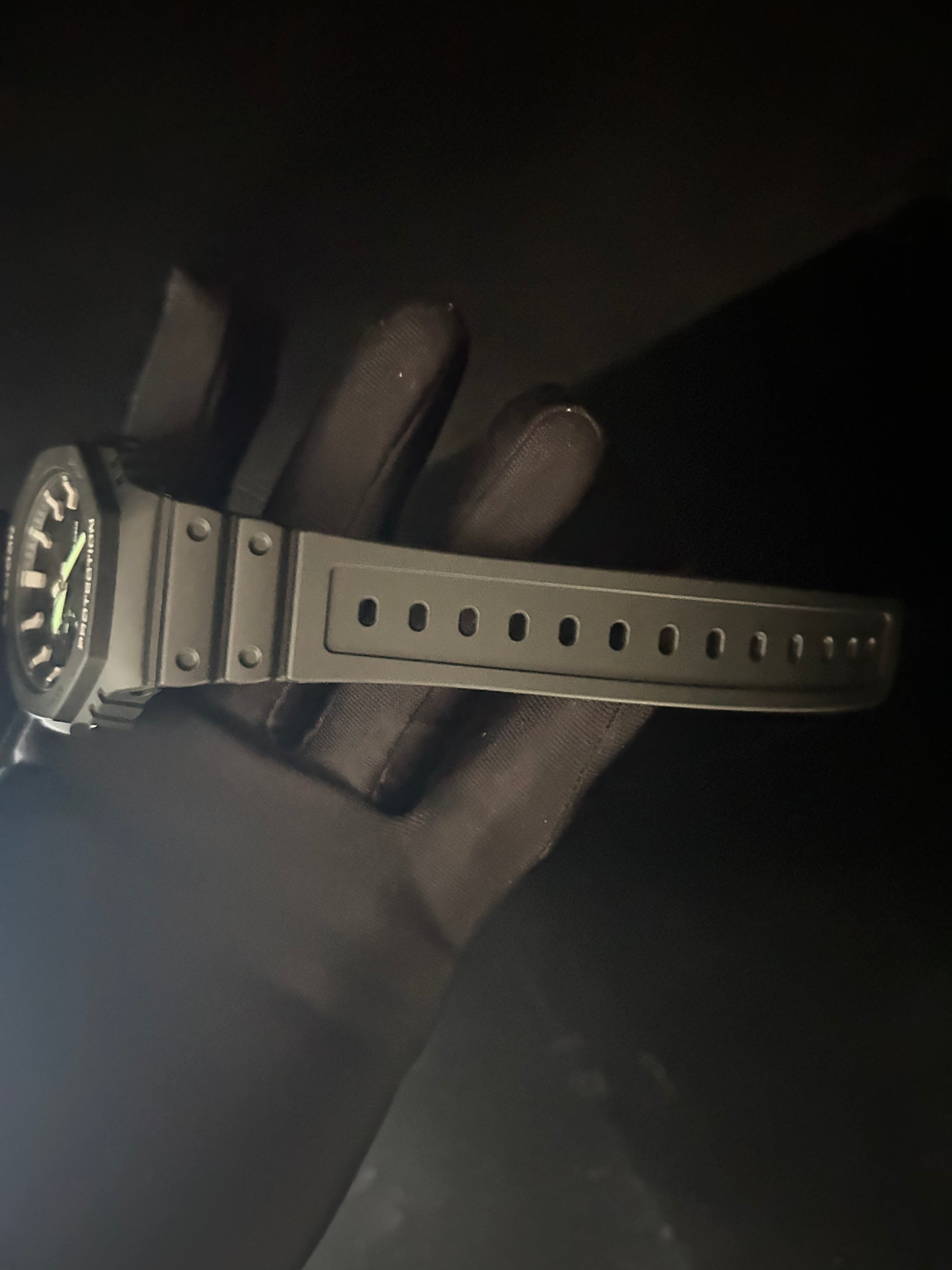 Black wristwatch with a textured strap held by a gloved hand against a dark background