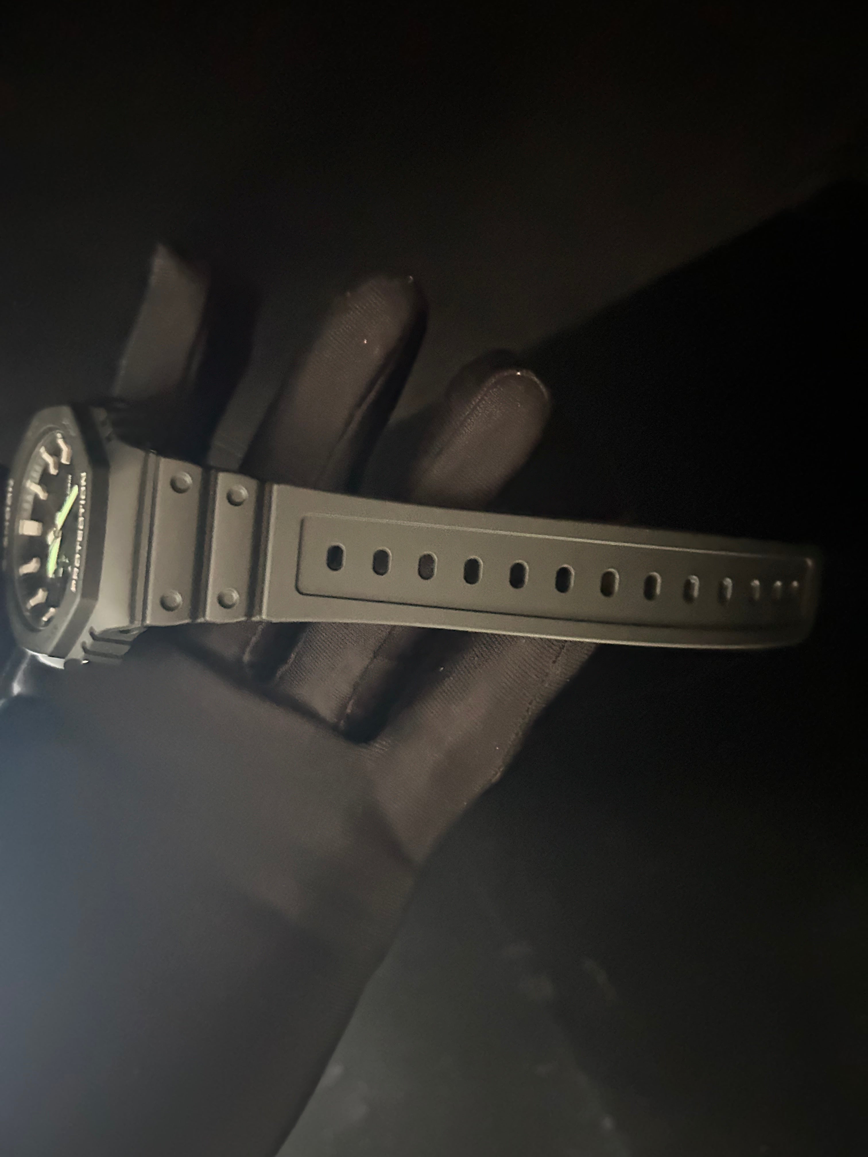 Black wristwatch with a textured strap held by a gloved hand against a dark background